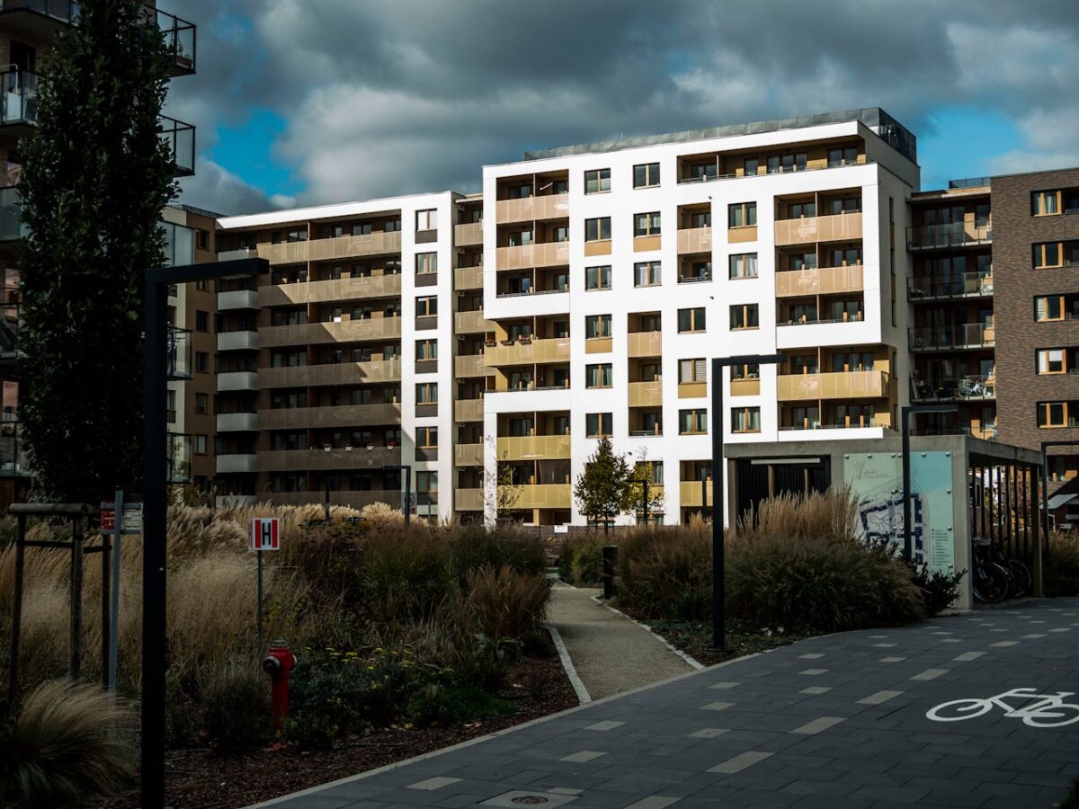 about-02 Contemporary apartment buildings surrounded by landscaped gardens and pathways under a cloudy sky.